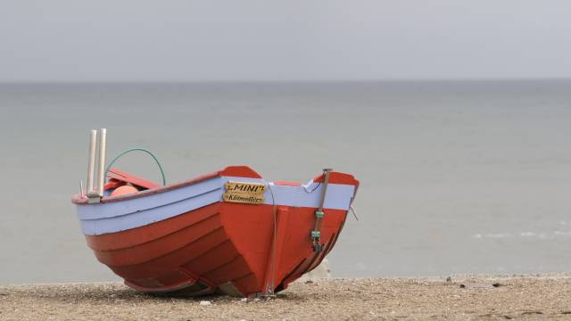 Ein kleines rotes Fischerboot liegt am Strand der Ostsee, im Hintergrund das ruhige graue Meer