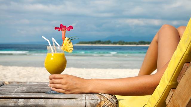 Exotischer gelber Cocktail mit Ananas und Blüte, gehalten von einer Person am Strand