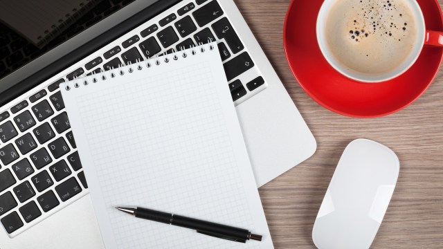 Laptop mit Notizblock, Stift, Computermaus und Kaffeetasse auf Schreibtisch