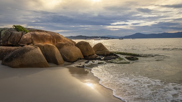 Sonnenuntergang am Strand mit großen Felsen und Blick aufs Meer