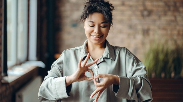 Junge Frau, die lächelnd ein Handzeichen in Gebärdensprache macht