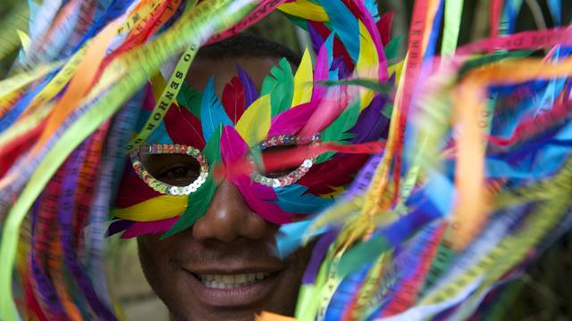 Mann trägt bunte Karnevalsmaske mit bunten Federn und lächelt zwischen den Verzierungen hervor