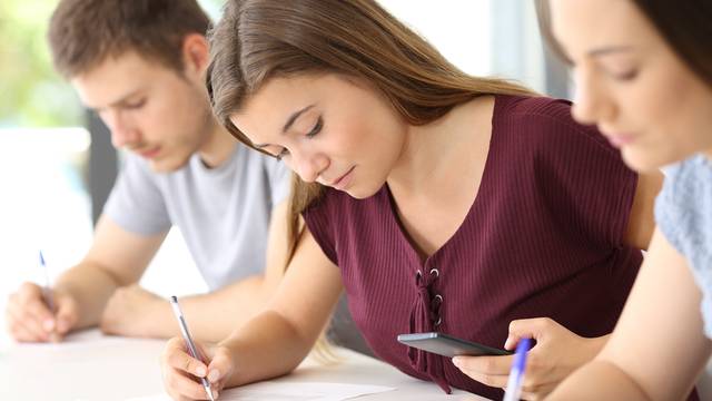 Junge Studentin schreibt konzentriert in einer Prüfung, hält Stift und Taschenrechner in der Hand