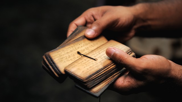 Hände halten alte Palmblatt-Handschrift mit eingravierten Schriftzeichen