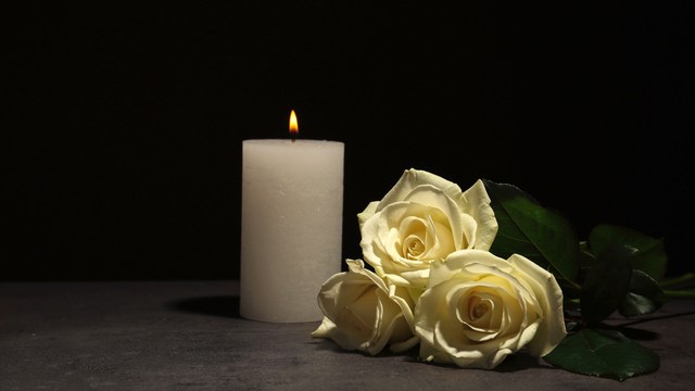 Weiße Kerze mit drei weißen Rosen vor dunklem Hintergrund