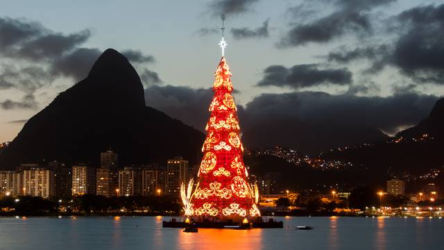 Beleuchteter Weihnachtsbaum schwimmt auf einem See in Rio de Janeiro bei Abenddämmerung, im Hintergrund Berge und Stadtlichter