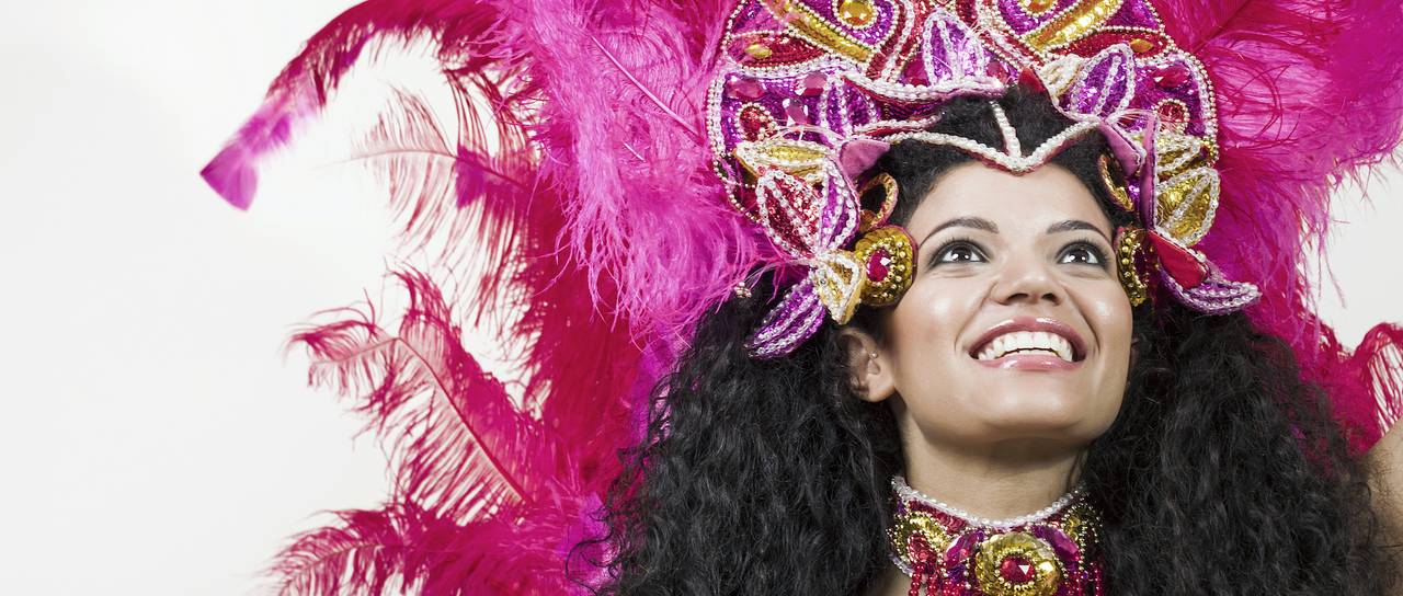 Junge Frau in farbenprächtigem Karnevalskostüm mit pinken Federn und glitzerndem Kopfschmuck, lächelnd ins Bild