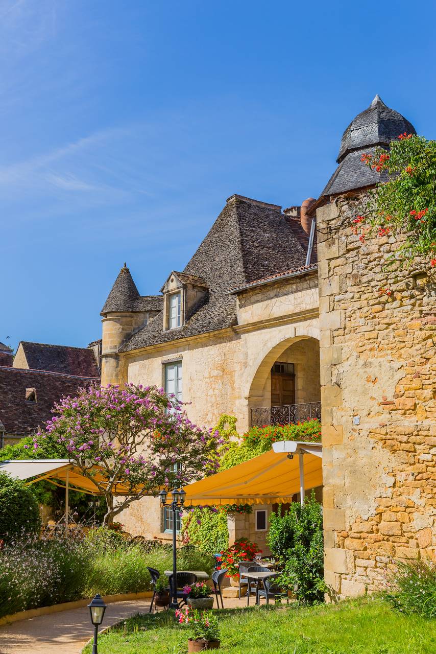 Historische Häuser in Sarlat-la-Canéda mit gelbem Stein, Garten und Markisen im Sonnenschein